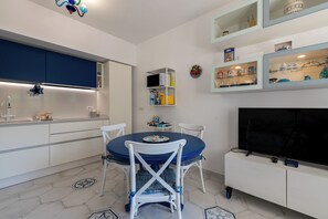 Una cucina moderna con mobili bianchi, un tavolo da pranzo blu e un televisore a schermo piatto.