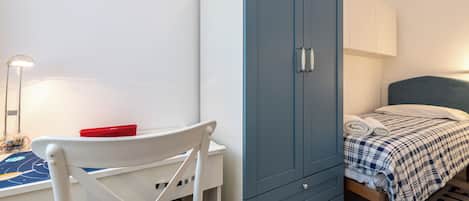 Een slaapkamer met een bed, een blauwe garderobe, een bureau met stoel en een lamp.