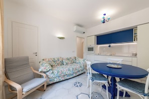 Ein kompakter Wohnbereich mit Sofa, Esstisch, Stuhl und Küchenzeile.