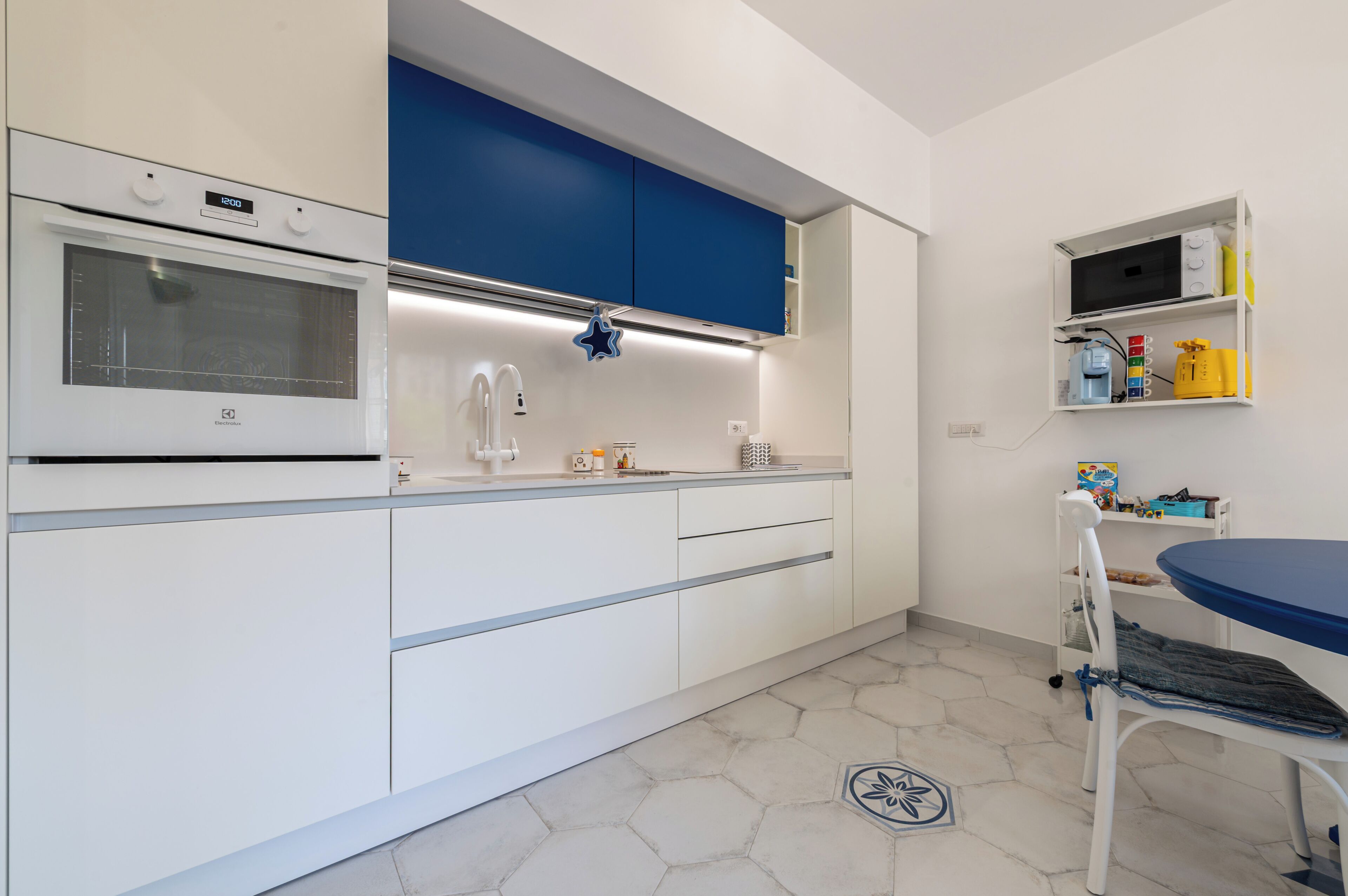 A modern kitchen with white cabinets, a blue countertop, and a microwave shelf.