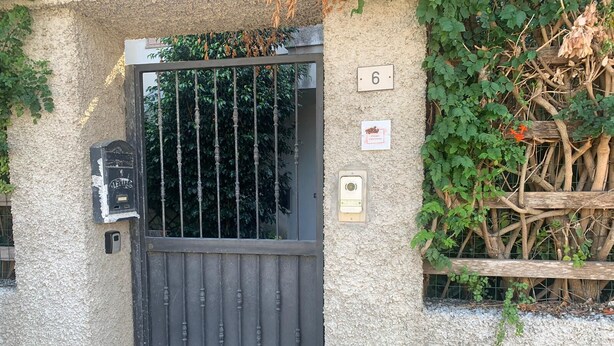 A textured wall with a number plaque '6', a metal gate, a mailbox, and a small sign with a logo. - Casa Corallo (Baratili San Pietro)