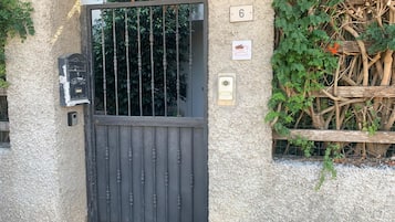 Parede texturizada com placa numérica '6', um portão de metal, uma caixa de correio e uma pequena placa com um logotipo.