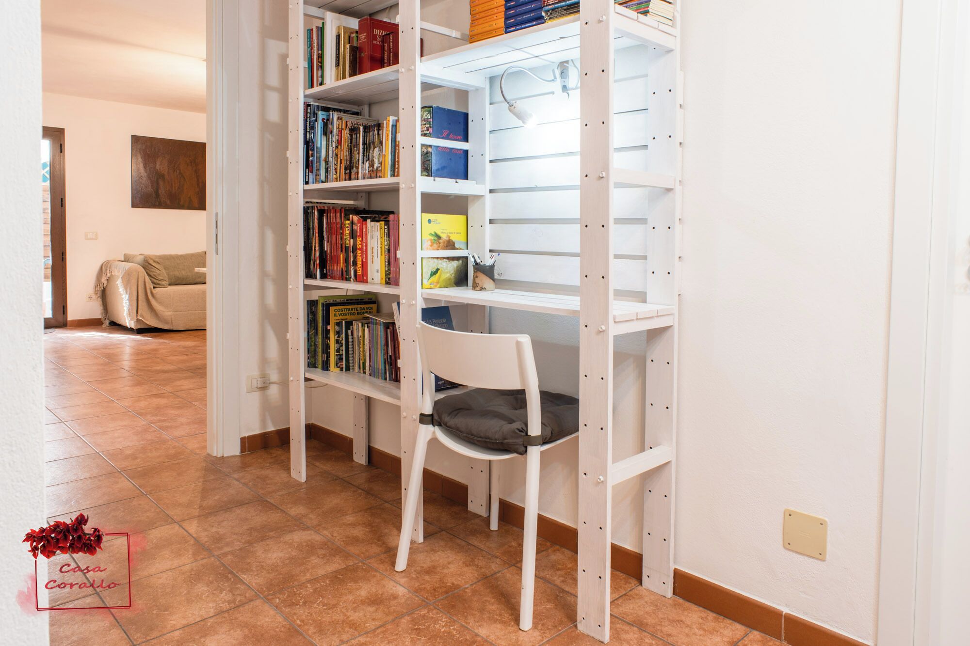 A room with a white bookshelf, a white chair, and a beige sofa.
