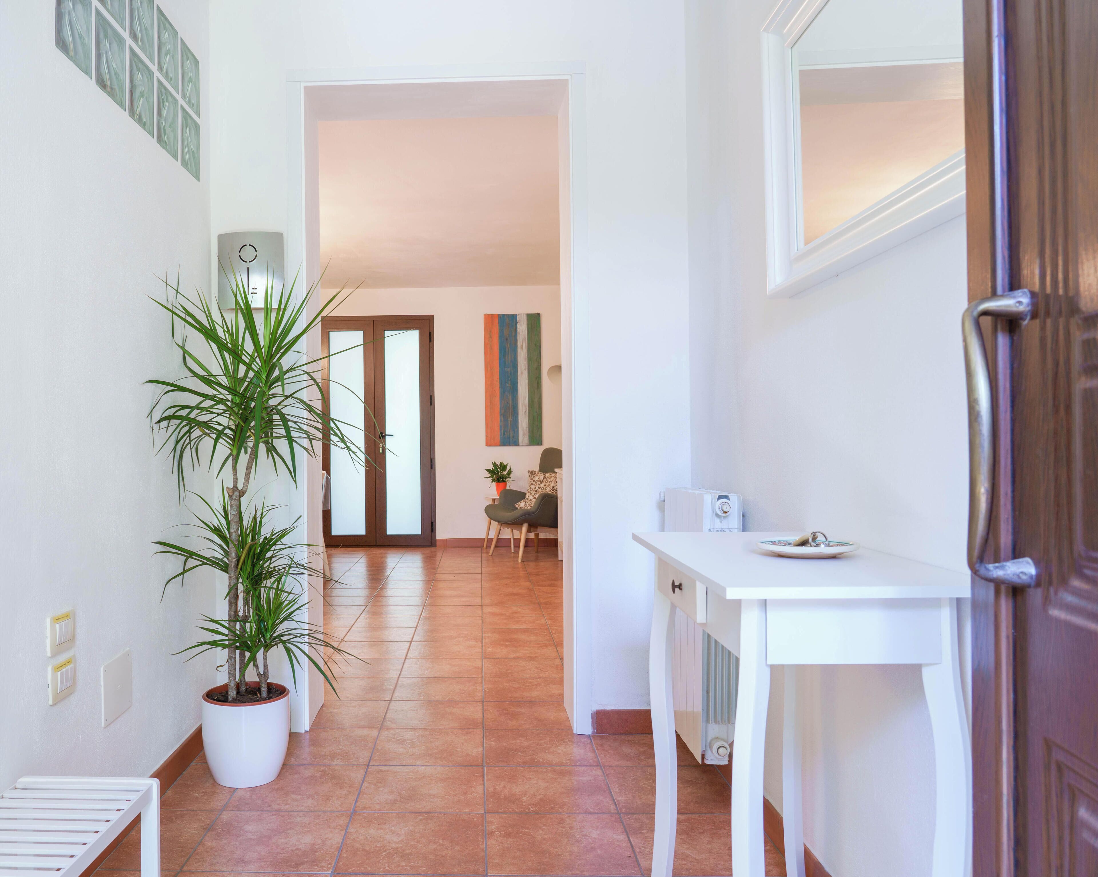A hallway with a white bench, potted plants, a white table with a radio, and a door.