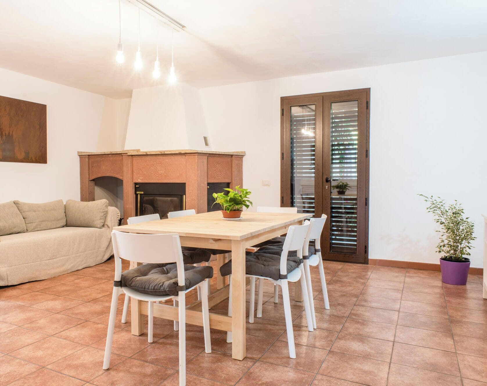 Uma sala de jantar com uma mesa e cadeiras de madeira, um sofá, uma lareira e uma porta com persianas.