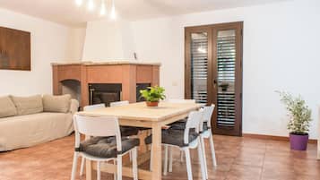 Uma sala de jantar com uma mesa e cadeiras de madeira, um sofá, uma lareira e uma porta com persianas.