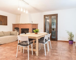 Uma sala de jantar com uma mesa e cadeiras de madeira, um sofá, uma lareira e uma porta com persianas.
