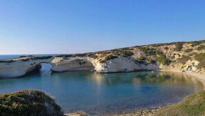 A coastal landscape with a natural arch formation, a sandy beach, and a clear blue sky. - Casa Corallo (Baratili San Pietro)