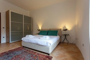 Un lit bien fait, avec des serviettes pliées, un oreiller vert et deux lampes de chevet.