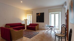 A living room with a red sofa, a brown armchair, a glass table with chairs, and a patterned rug. - Vico Santa Maria del Pozzo 9 (Naples)