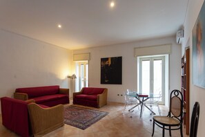 Ein Wohnzimmer mit einem roten Sofa, einem braunen Sessel, einem Glastisch mit Stühlen und einem gemusterten Teppich.