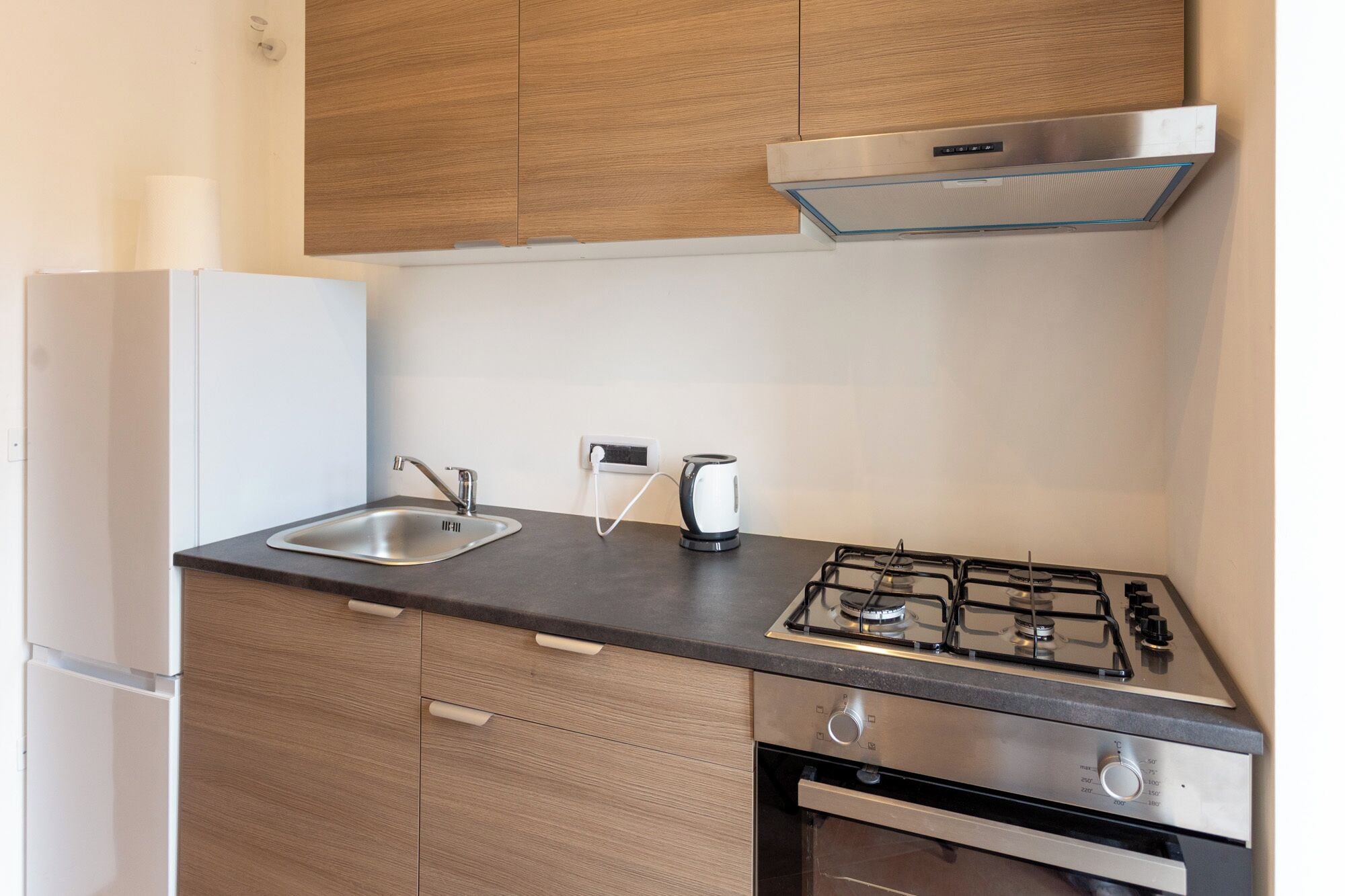 A compact kitchen with a gas stove, a kettle, and a built-in oven.