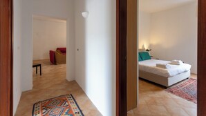 A hotel room with a bed, a small seating area with a chair and a table, and a hallway leading to another room. - Vico Santa Maria del Pozzo 9 (Naples)