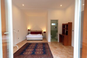 A hotel room with a bed, a small bedside table, a nightstand, a wooden cabinet, and a bathroom visible through an open door. - Vico Santa Maria del Pozzo 9 (Naples)