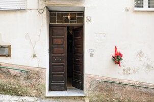 A wooden door with a window above it, a small sign on the wall, and a red flower decoration.