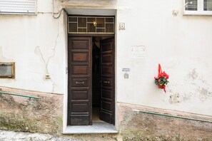 Una puerta de madera con un ventanal encima, una pequeña señal en la pared y un adorno floral rojo.