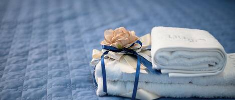 A neatly folded white towel with a blue ribbon and a peach-colored flower on a blue quilted bedspread.