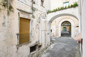 A narrow cobblestone street with an arched entrance and a shuttered window.