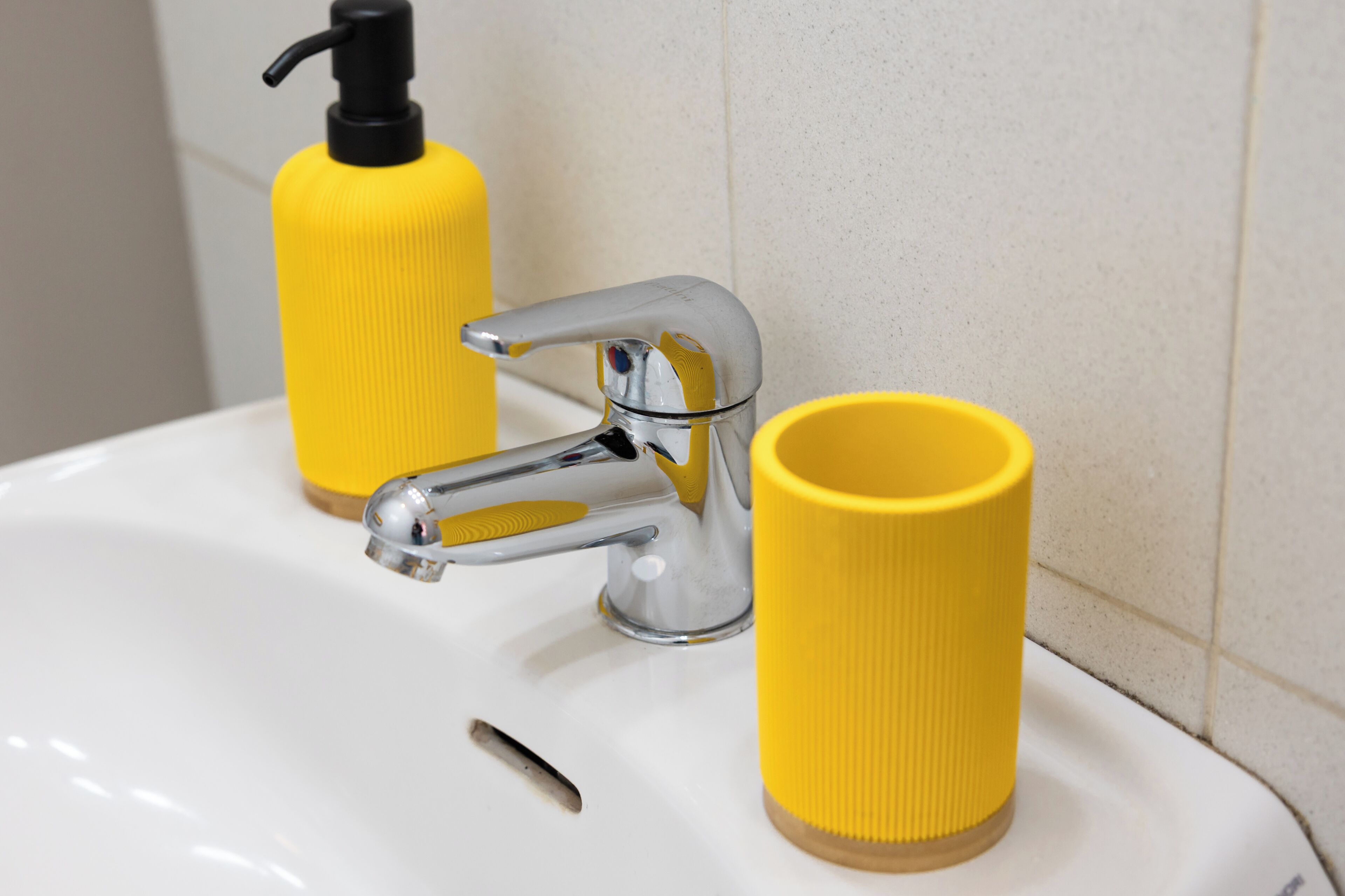 Un lavamanos con grifo cromado, dispensador de jabón amarillo y taza amarilla.