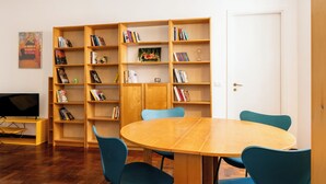 Una habitación con una mesa de comedor de madera, sillas azules, una estantería y un televisor sobre un mueble.