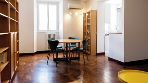 Una habitación con piso de madera, una mesa redonda con sillas, una estantería y un radiador.