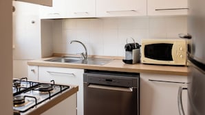 Una cocina compacta equipada con estufa a gas, lavavajillas, microondas y pileta.