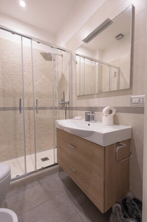A modern bathroom with a glass shower enclosure, a wooden vanity with a sink, and a mirror above the vanity. - Civico 79 (Naples)