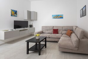 Ein modernes Wohnzimmer mit einem beigen Sofa, einem schwarzen Couchtisch, einem Flachbildfernseher und einer weißen Unterhaltungsanlage.