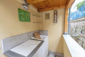 Eine kleine Küche mit Holzboden, einer weißen Arbeitsplatte und einem Spülbecken. An der Wand befinden sich zwei Regale und ein dekorativer Teller.