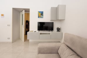 A modern living room with a flat-screen TV on a white entertainment unit, a beige sofa, and a door leading to another room. - Civico 79 (Naples)