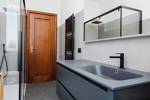 A modern bathroom with a large sink, a wooden door, a towel rack, and a mirror. - Azalee Urban Nest (Rome)