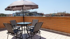Eine Dachterrasse mit Tisch, vier Stühlen und Sonnenschirm, mit Blick auf umliegende Gebäude.