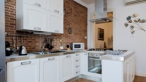 Una cocina moderna con armarios blancos, pared de ladrillo, electrodomésticos de acero inoxidable y un piso con patrón de espiga.