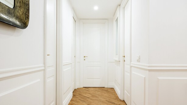 Un pasillo con paredes blancas y suelo de madera que conduce a una puerta cerrada.