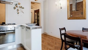 Una cocina con armarios blancos, una estufa y un comedor con mesa y sillas de madera.