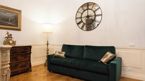 Una habitación con un sofá verde, un aparador de madera, un reloj de pared grande y una lámpara.