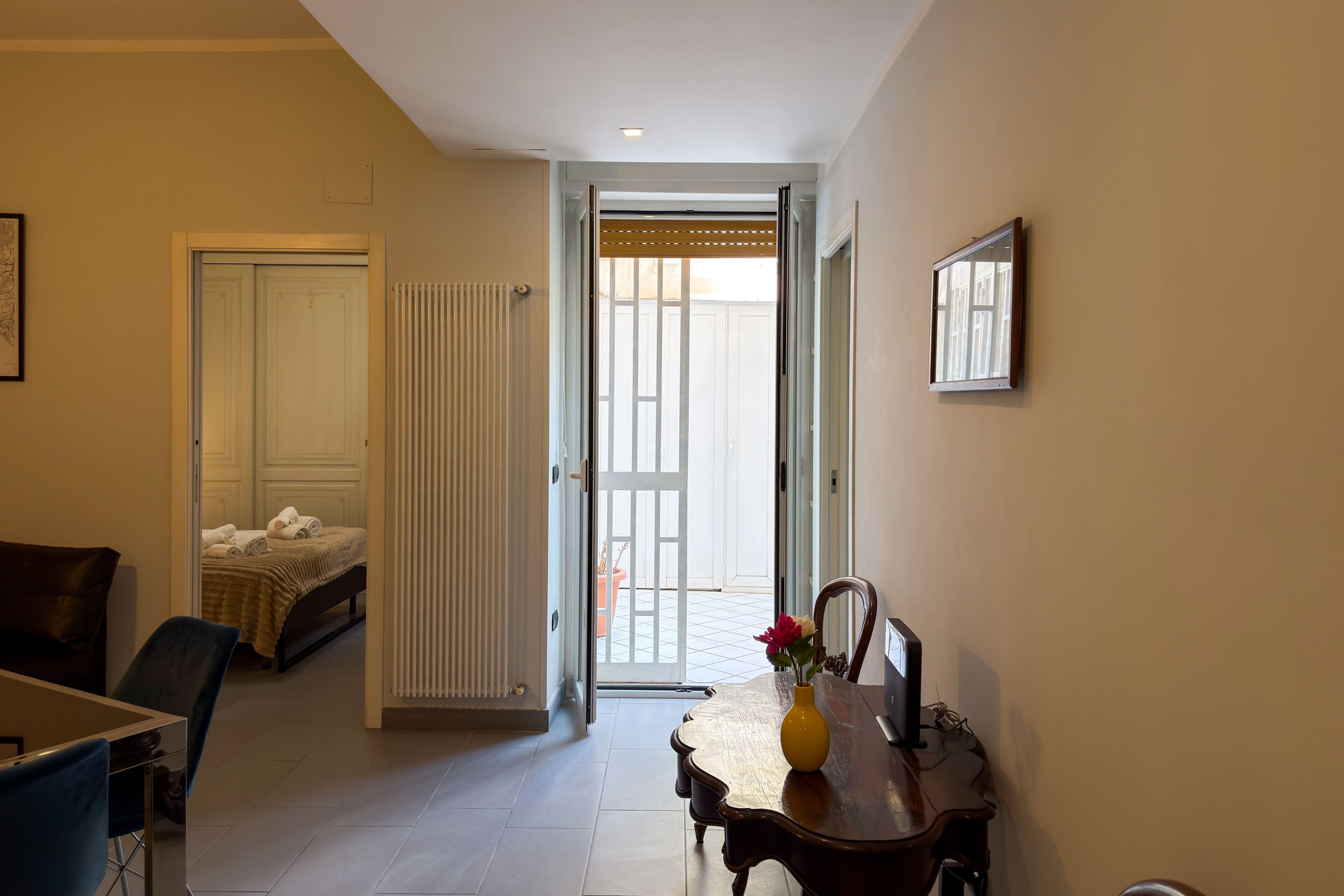 Een hotelkamer met een bed, een eettafel met een vaas, een stoel en een deur naar een balkon.