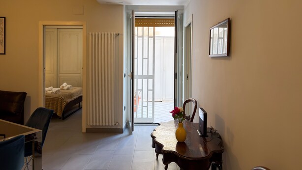 Ein Hotelzimmer mit Bett, einem Esstisch mit Vase, einem Stuhl und einer Tür, die auf einen Balkon führt.