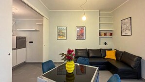 Ein modernes Wohnzimmer mit einem Esstisch mit Glasplatte, einem schwarzen Ledersofa und einer Küche im Hintergrund.