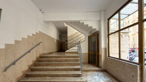Eine Treppe mit Metallgeländer, Marmorstufen und Blick durch ein großes Fenster nach draußen.