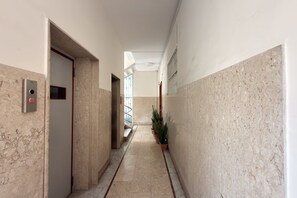 A hallway with a marble floor, a door with a red handle, a potted plant, and a light fixture on the ceiling. - Riviera di Chiaia 207 - 1° Piano (Naples)