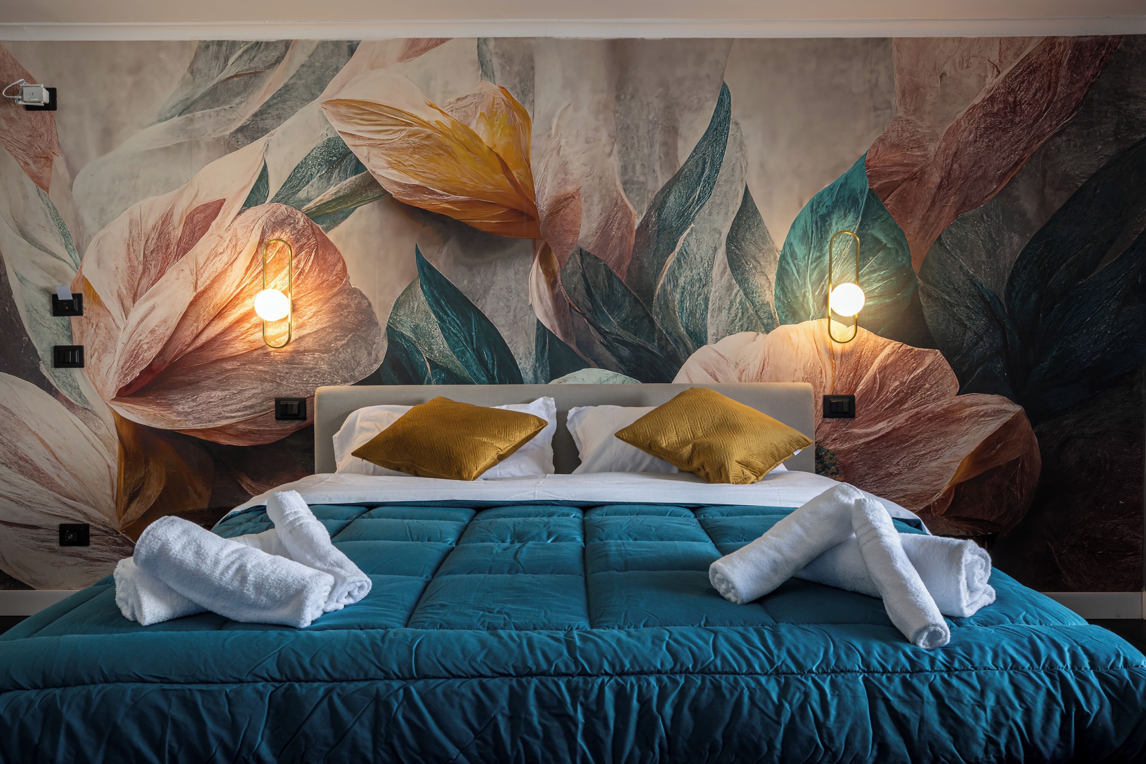 A bed with teal bedding, two gold pillows, and a white towel.