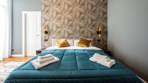 A hotel room with a teal bedspread, two gold pillows, a white door, and a textured wall. - Zapata Relais - Chiaia (Naples)