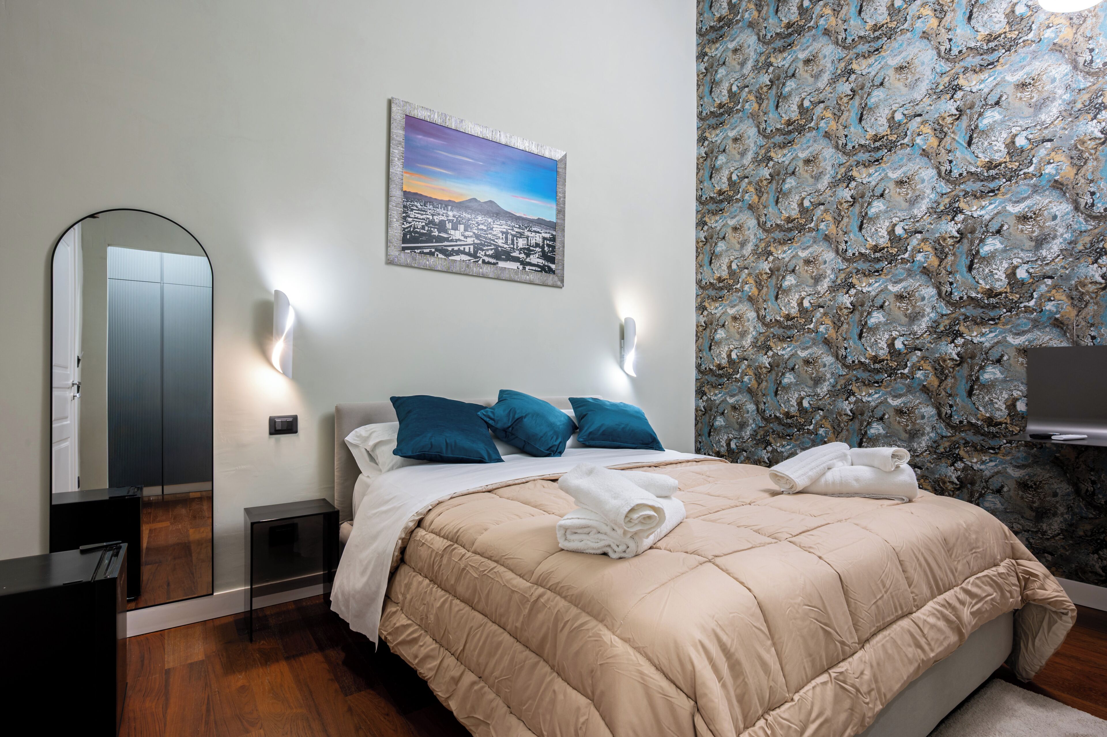 Un dormitorio con una cama, almohadas, un cuadro, un espejo y una pared con textura.