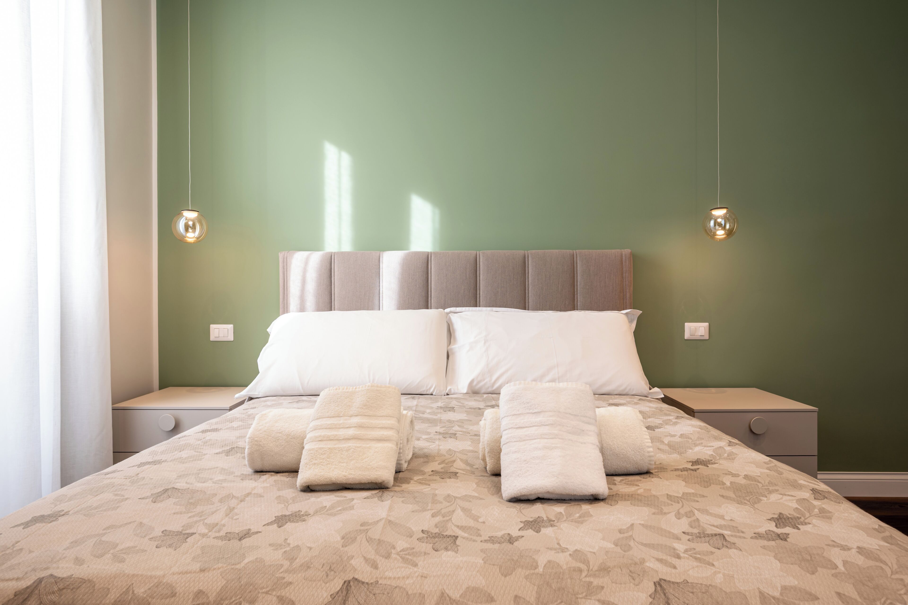 Una cama bien hecha con almohadas y toallas, dos mesitas de noche y lámparas colgantes.