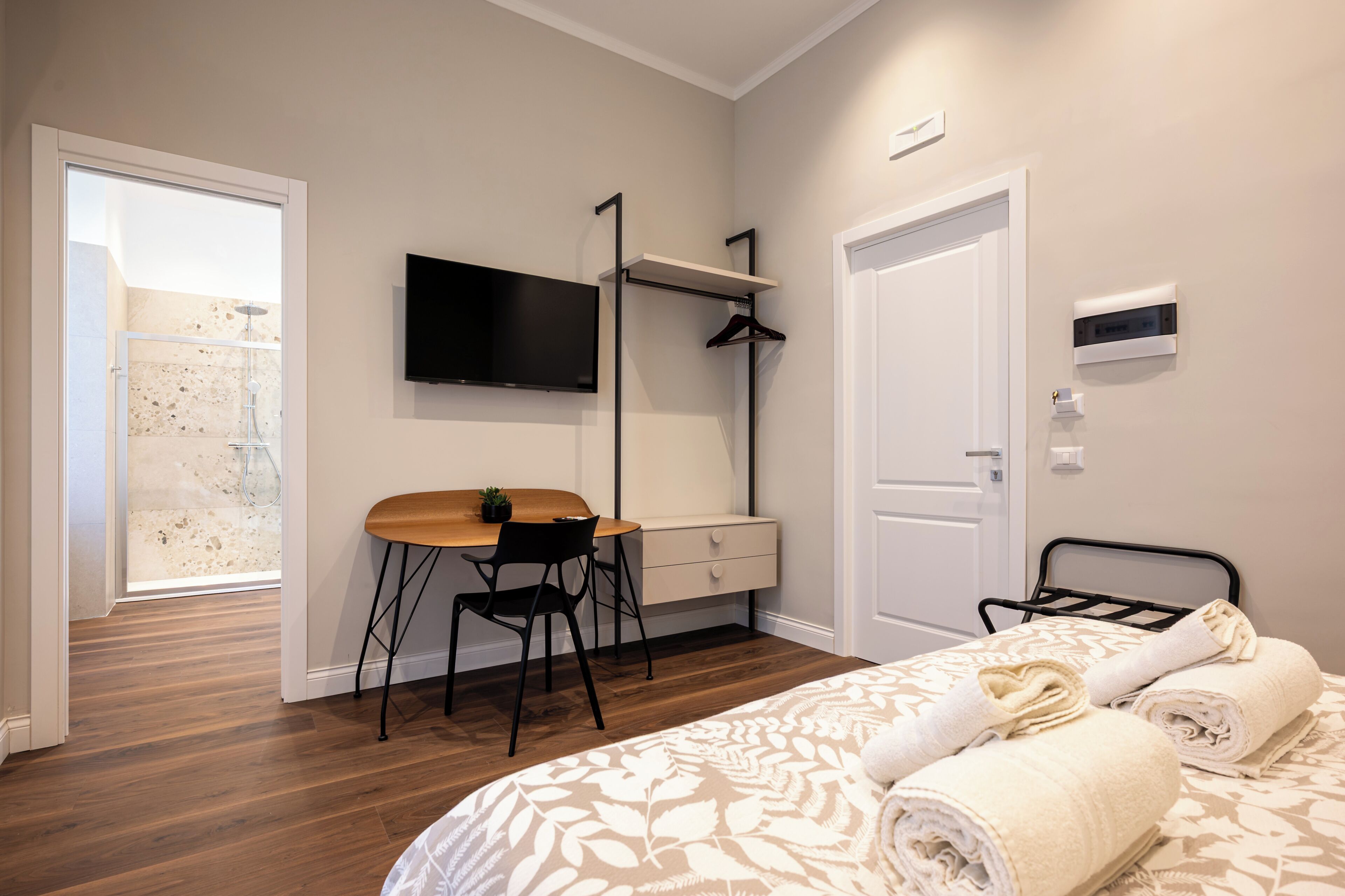 Un dormitorio con cama, escritorio, silla, televisión, armario y baño con ducha.