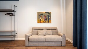 A living room with a beige sofa, a painting of a couple on a balcony, and a dark blue curtain. - Casa Eva - 18 (Naples)