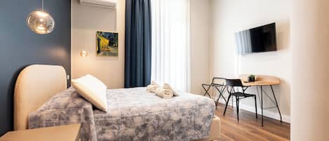 A modern hotel room with a bed, a desk, a chair, a TV, and an air conditioning unit.