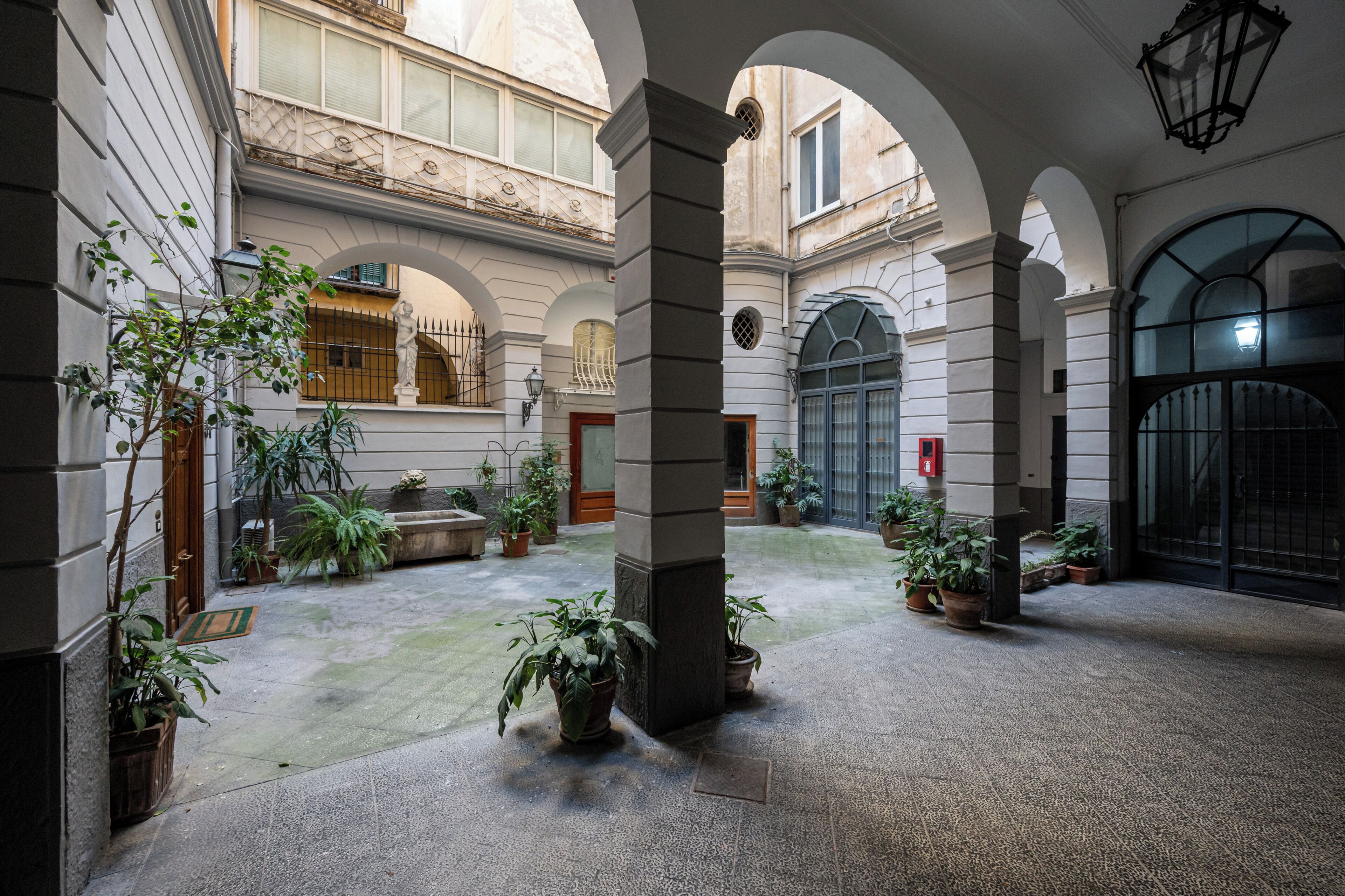 A courtyard with arches, potted plants, and a stone column.