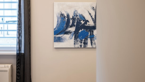 Quarto com cama, ar-condicionado fixado na parede e uma grande pintura abstrata.